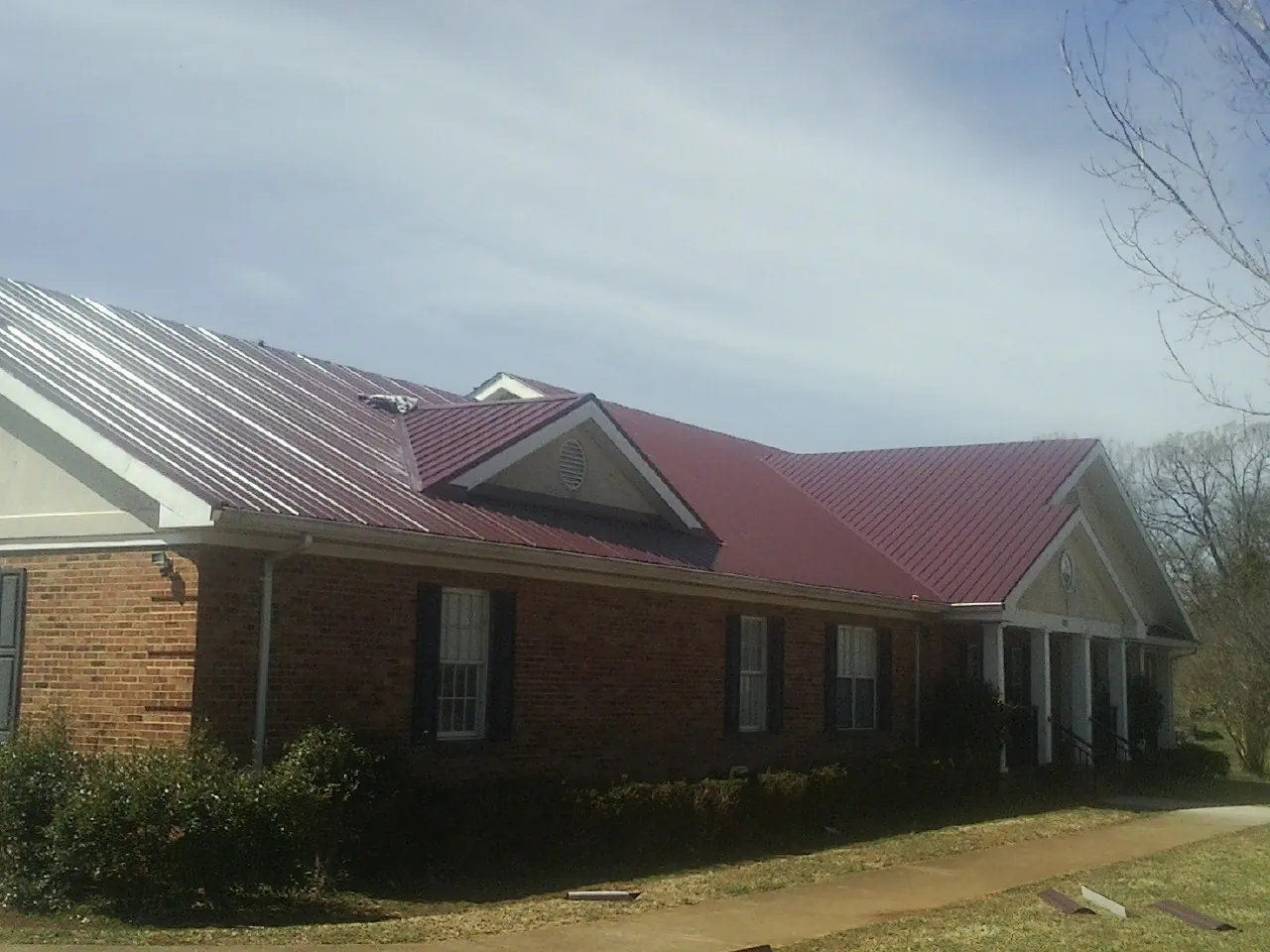 Red metal roof with gabled entries on a long brick building, from a Hail Damage Roof Repair job in Deale