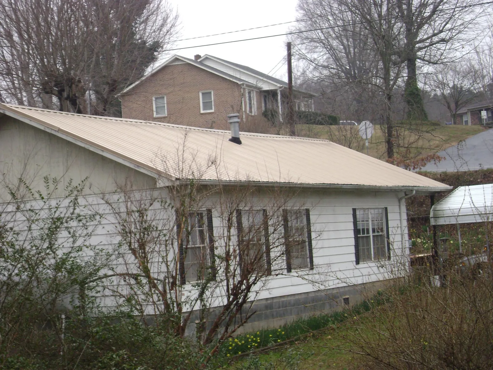 Tan metal roof on a white sided house set into a hillside — Commercial Roofing by Roofing Brothers in Deale